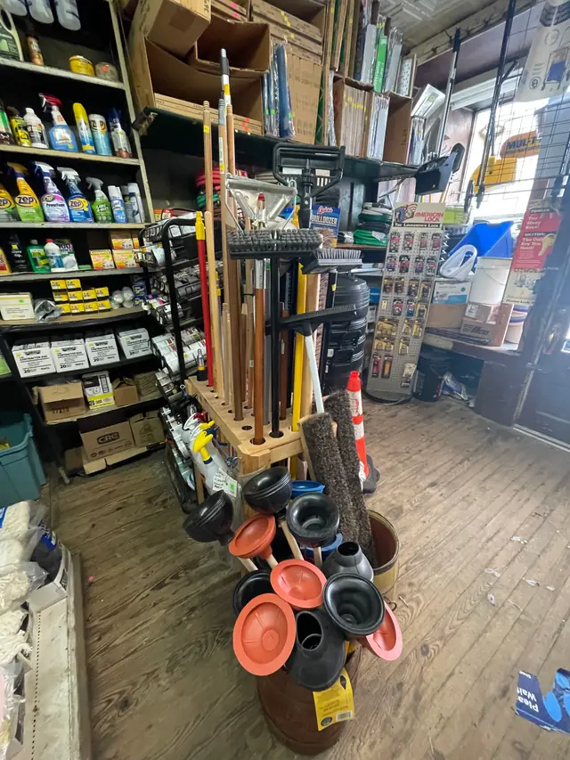 Brooms, mops and plungers standing beside shelves of cleaning supplies